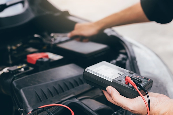 Technician checking charge of car battery with multimeter